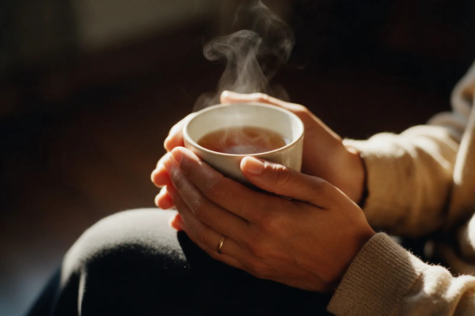 Mãos seguram uma xícara de chá quente, com o vapor subindo na luz dourada